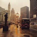 A rainy day scene in downtown Chicago featuring urban architecture, a bus, and the city skyline.